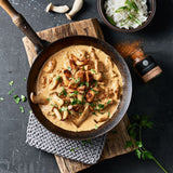 Hähnchenpfanne mit Pilzen in einer gußeisernen Pfanne auf einem Holzbrett.