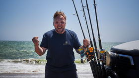 Der Ankerkraut Gründer steht vor dem offenen Meer und freut sich. An der Seite stehen verschiedene Angeln an einer Motorhaube