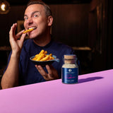 Tim Raue beißt in eine Pommes, während vor ihm das Ankerkraut Smoky Fries Gewürz im Korkenglas steht.