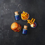 Ein saftiger Burger sowie knusprige Pommes aus der Vogelperspektive, daneben Ankerkraut Smoky Fries sowie Spicy Hack im Korkenglas.