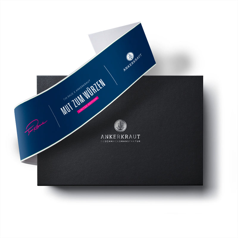 Tim Raue Geschenk Box aus schwarzem Karton mit diagonaler Banderole.