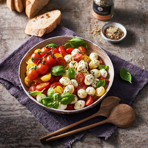 Caprese Bowl in einem tiefen Teller, daneben Brot und ein Schälchen mit Gewürzen.